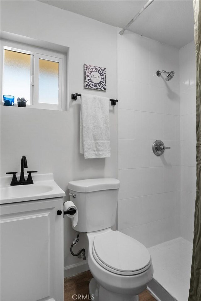 bathroom with toilet, a tile shower, hardwood / wood-style floors, and vanity