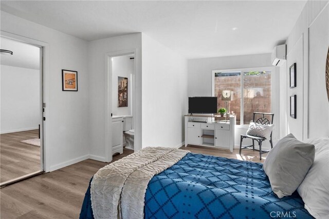 bedroom featuring ensuite bath, an AC wall unit, and wood-type flooring