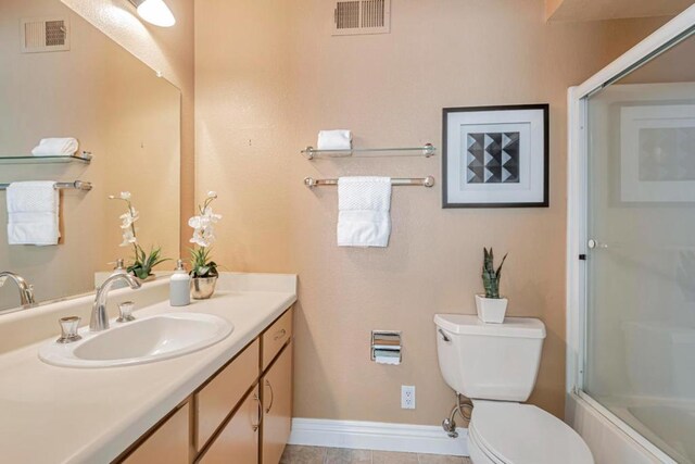 full bathroom featuring toilet, vanity, tile patterned flooring, and enclosed tub / shower combo