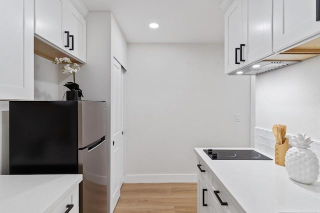 kitchen featuring light wood-type flooring, black electric stovetop, white cabinets, and stainless steel refrigerator