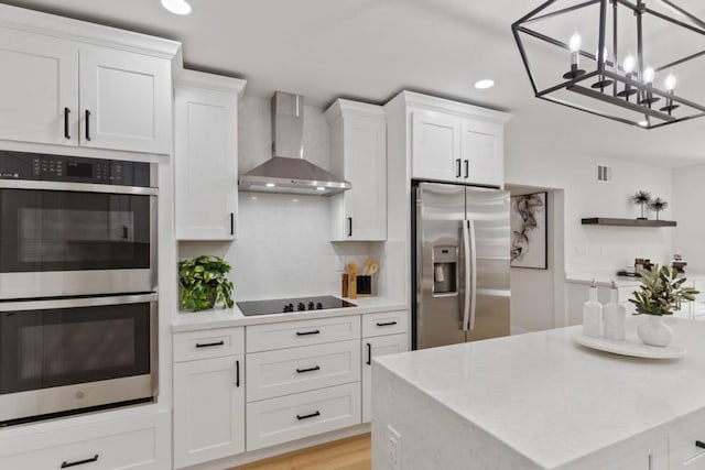 kitchen with decorative light fixtures, wall chimney range hood, light hardwood / wood-style floors, white cabinetry, and appliances with stainless steel finishes