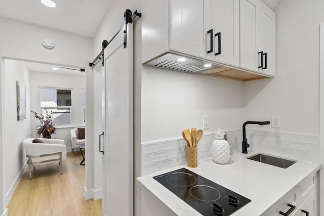 kitchen featuring black electric stovetop, a barn door, white cabinets, and sink