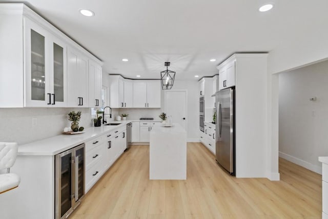 kitchen with decorative light fixtures, a kitchen island, appliances with stainless steel finishes, white cabinets, and beverage cooler