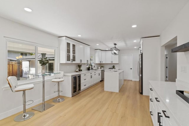 kitchen featuring beverage cooler, a center island, appliances with stainless steel finishes, white cabinetry, and hanging light fixtures