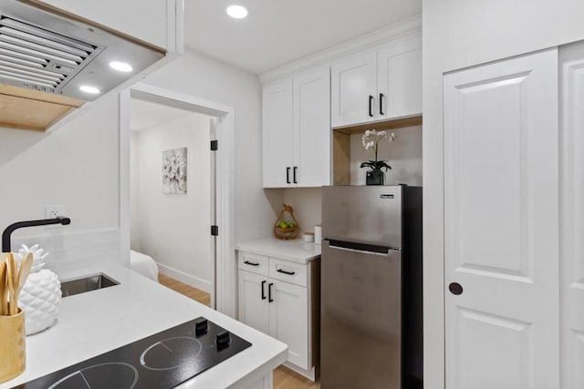 kitchen with white cabinets, light hardwood / wood-style floors, sink, stainless steel fridge, and black electric cooktop