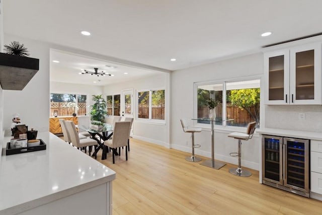 dining space with wine cooler, a healthy amount of sunlight, bar, and light hardwood / wood-style flooring