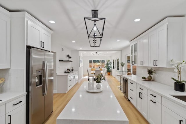 kitchen featuring stainless steel refrigerator with ice dispenser, white cabinets, hanging light fixtures, and a center island