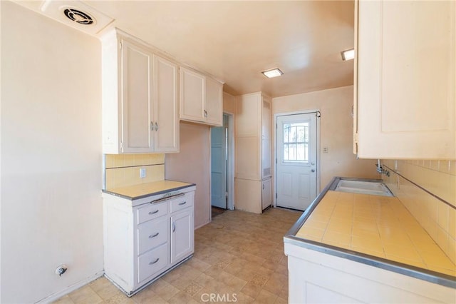 kitchen featuring sink, white cabinetry, backsplash, and tile counters