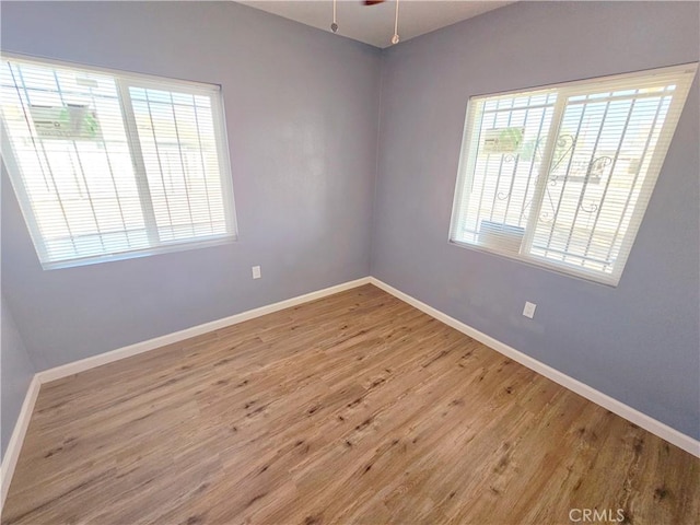 empty room with ceiling fan, a wealth of natural light, and light wood-type flooring