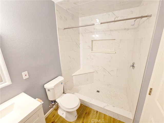 bathroom with wood-type flooring, tiled shower, vanity, and toilet