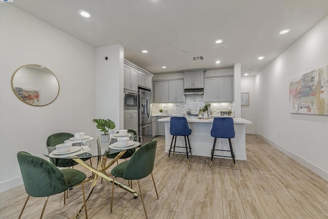 kitchen featuring a breakfast bar area, built in microwave, stainless steel refrigerator with ice dispenser, and gray cabinets