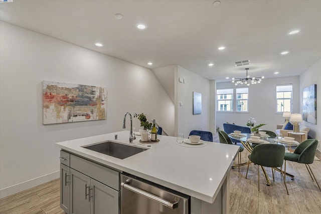 kitchen featuring light hardwood / wood-style flooring, dishwasher, sink, gray cabinets, and a center island with sink