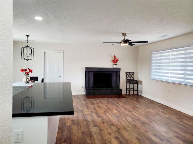 unfurnished living room with a textured ceiling, ceiling fan with notable chandelier, and dark hardwood / wood-style floors