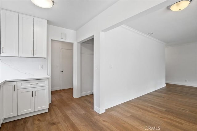 interior space featuring decorative backsplash, crown molding, white cabinetry, and light hardwood / wood-style flooring