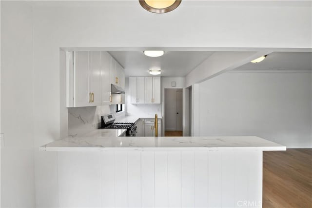 kitchen with stainless steel range, decorative backsplash, white cabinets, and kitchen peninsula