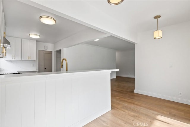 kitchen featuring white cabinetry, kitchen peninsula, range hood, pendant lighting, and light hardwood / wood-style flooring