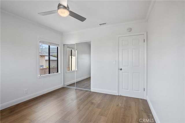 unfurnished bedroom featuring ceiling fan, a closet, wood-type flooring, and crown molding