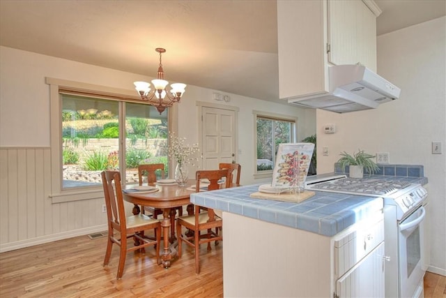 kitchen with white cabinets, white stove, exhaust hood, and tile countertops