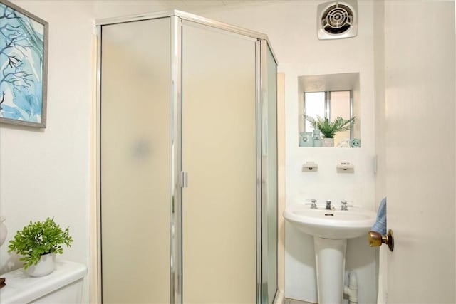 bathroom featuring toilet, a shower with door, and sink