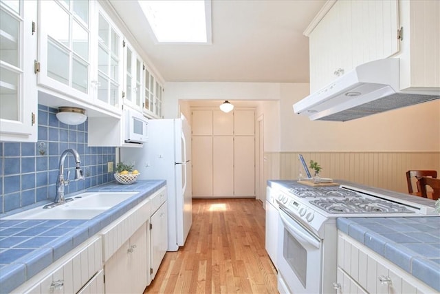 kitchen featuring range hood, tile countertops, white cabinetry, and white appliances