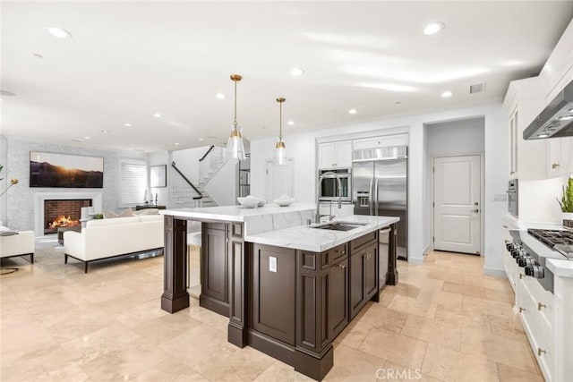 kitchen with dark brown cabinetry, white cabinetry, stainless steel appliances, hanging light fixtures, and a large fireplace