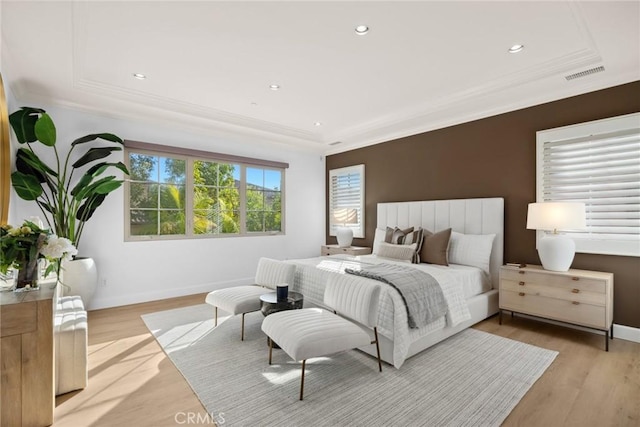 bedroom featuring crown molding, light hardwood / wood-style flooring, and a tray ceiling