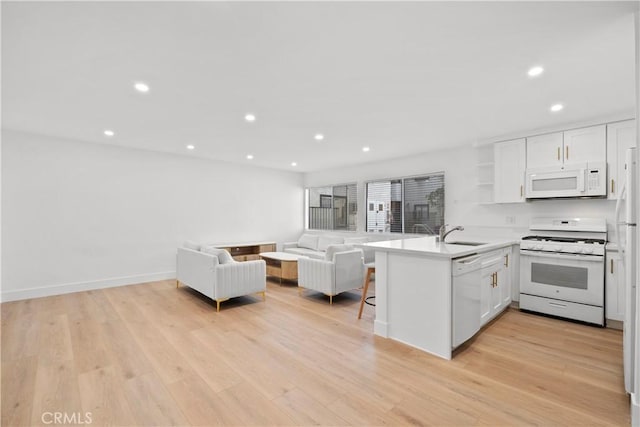 kitchen with white appliances, white cabinets, sink, kitchen peninsula, and light wood-type flooring