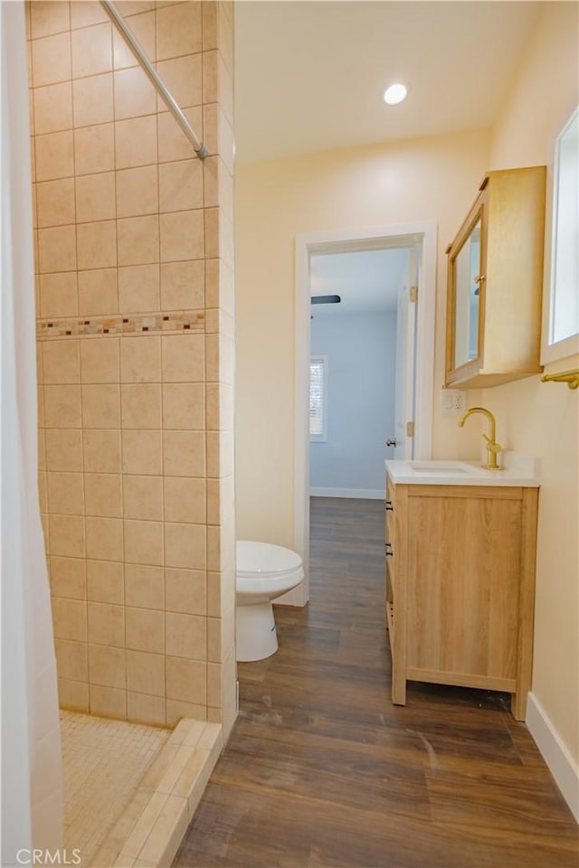 bathroom with toilet, vanity, tiled shower, and hardwood / wood-style flooring