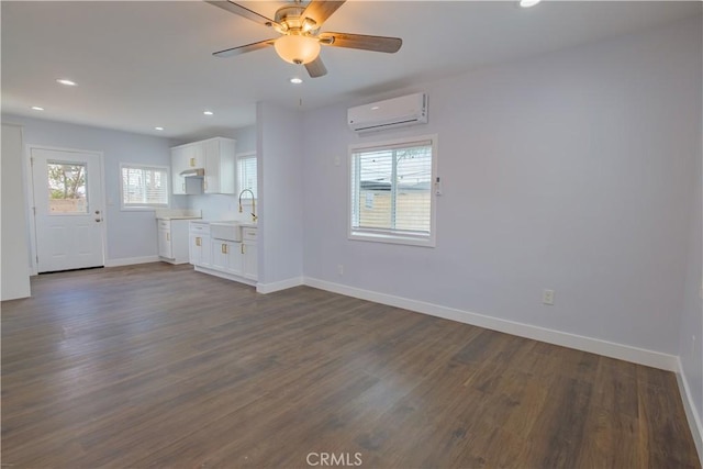 unfurnished living room featuring a wall unit AC, dark wood-type flooring, sink, and ceiling fan