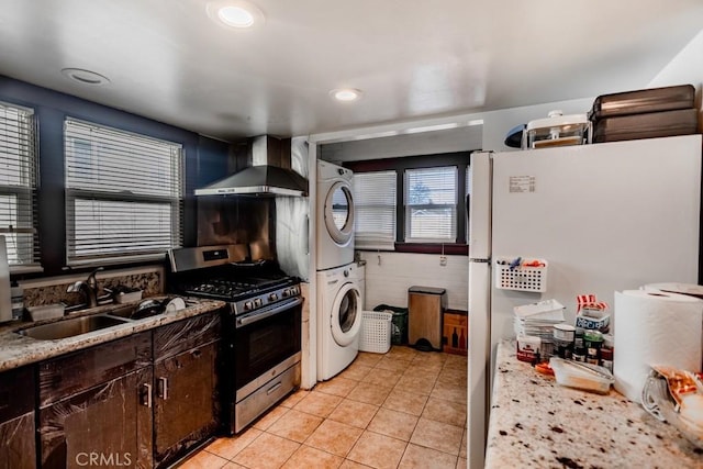 kitchen with wall chimney exhaust hood, stacked washer / drying machine, white fridge, sink, and stainless steel range with gas stovetop