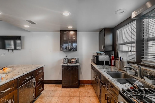 kitchen with light stone countertops, light tile patterned floors, dark brown cabinets, and sink