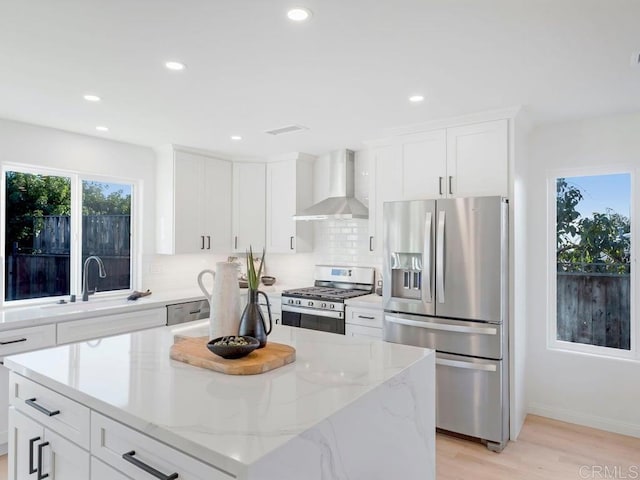 kitchen with appliances with stainless steel finishes, light stone counters, wall chimney exhaust hood, sink, and white cabinets