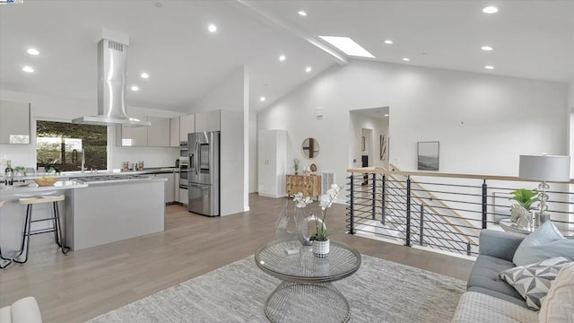 living room with high vaulted ceiling, light wood-type flooring, and a skylight