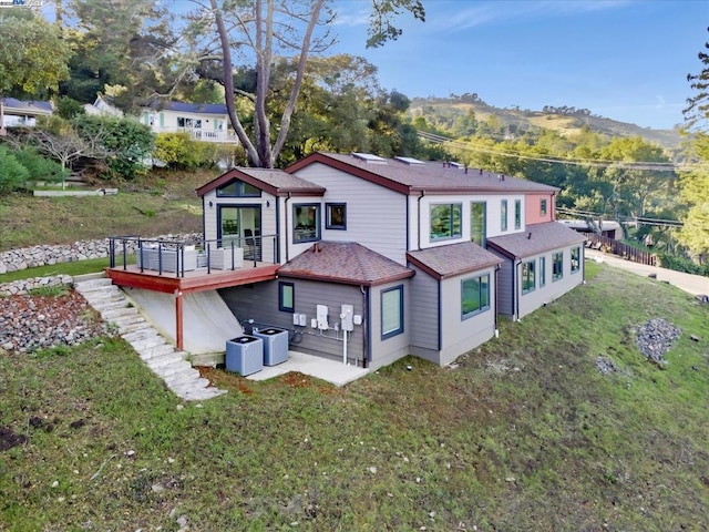 rear view of house with central AC unit, a lawn, and a deck with mountain view