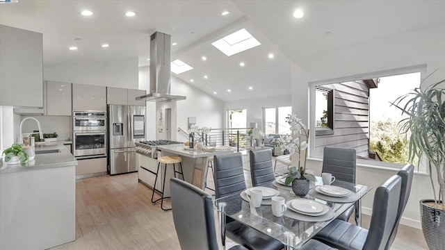 dining space featuring a skylight, light hardwood / wood-style flooring, high vaulted ceiling, and sink