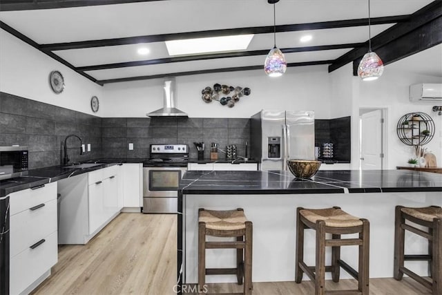 kitchen with decorative light fixtures, a center island, a breakfast bar area, stainless steel appliances, and wall chimney exhaust hood