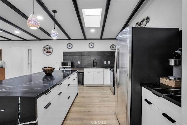 kitchen with white cabinets, decorative light fixtures, a skylight, stainless steel appliances, and backsplash