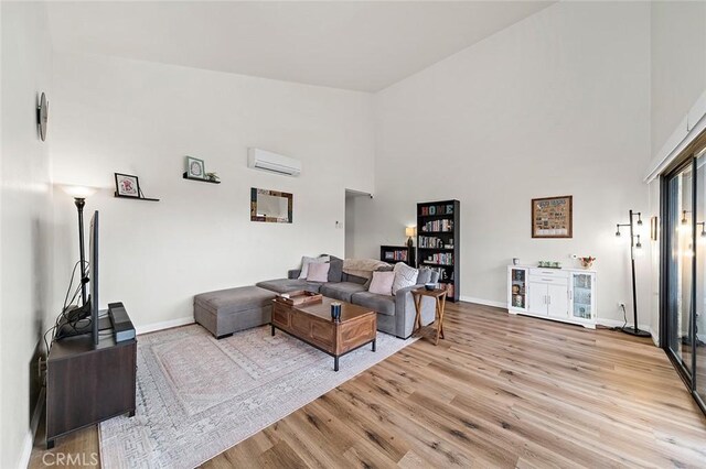 living room with an AC wall unit, a high ceiling, and light hardwood / wood-style floors