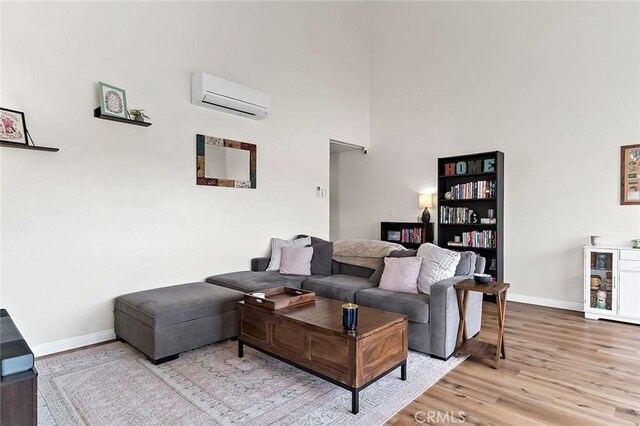 living room featuring a high ceiling, light hardwood / wood-style flooring, and a wall mounted air conditioner