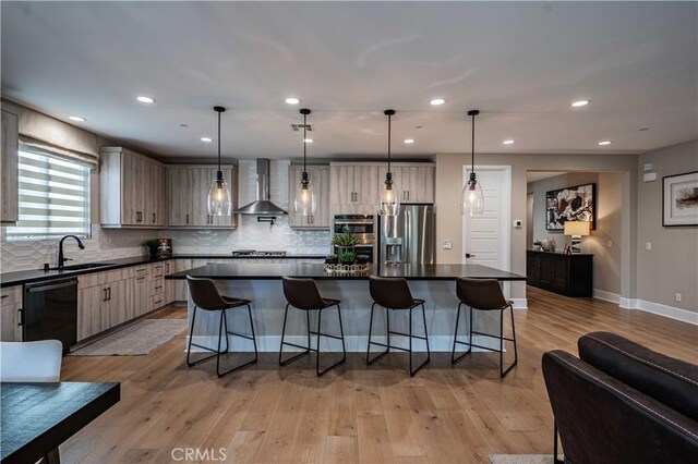 kitchen featuring appliances with stainless steel finishes, a center island, wall chimney exhaust hood, decorative light fixtures, and sink