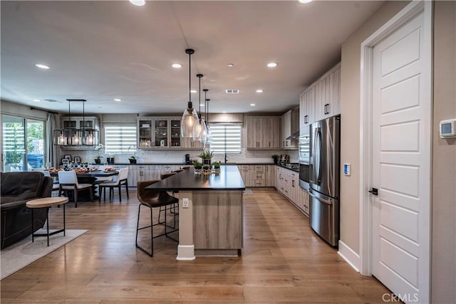 kitchen featuring backsplash, pendant lighting, a center island, stainless steel refrigerator, and light hardwood / wood-style flooring