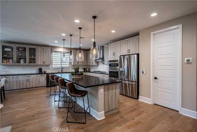 kitchen featuring stainless steel appliances, tasteful backsplash, decorative light fixtures, a kitchen island, and wall chimney exhaust hood