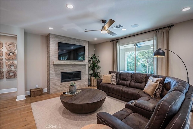 living room featuring ceiling fan, a tile fireplace, and light hardwood / wood-style flooring