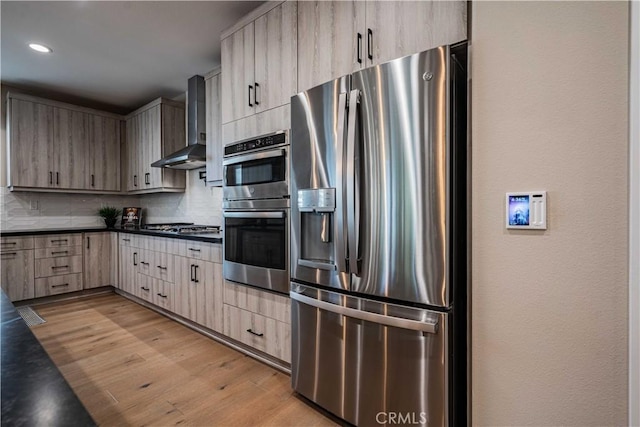 kitchen featuring backsplash, wall chimney range hood, light hardwood / wood-style flooring, stainless steel appliances, and light brown cabinetry