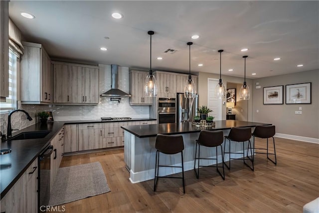 kitchen with a center island, wall chimney range hood, stainless steel appliances, sink, and hanging light fixtures