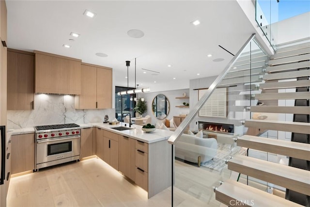 kitchen featuring light brown cabinetry, sink, hanging light fixtures, kitchen peninsula, and premium range