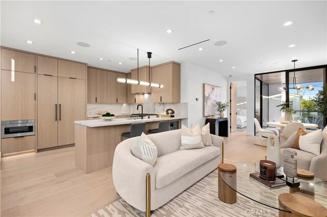 living room featuring sink, expansive windows, a notable chandelier, and light wood-type flooring