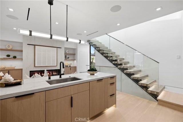 kitchen featuring sink, light stone counters, hanging light fixtures, light brown cabinets, and a large fireplace