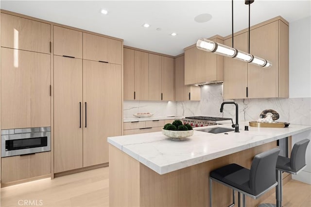 kitchen with light stone countertops, decorative light fixtures, tasteful backsplash, light brown cabinetry, and sink