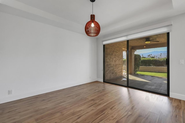 empty room with ceiling fan, wood-type flooring, and a tray ceiling